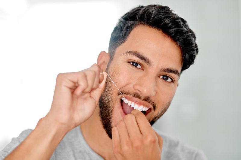 Man flossing teeth as part of caring for a dental crown in Wetherill Park