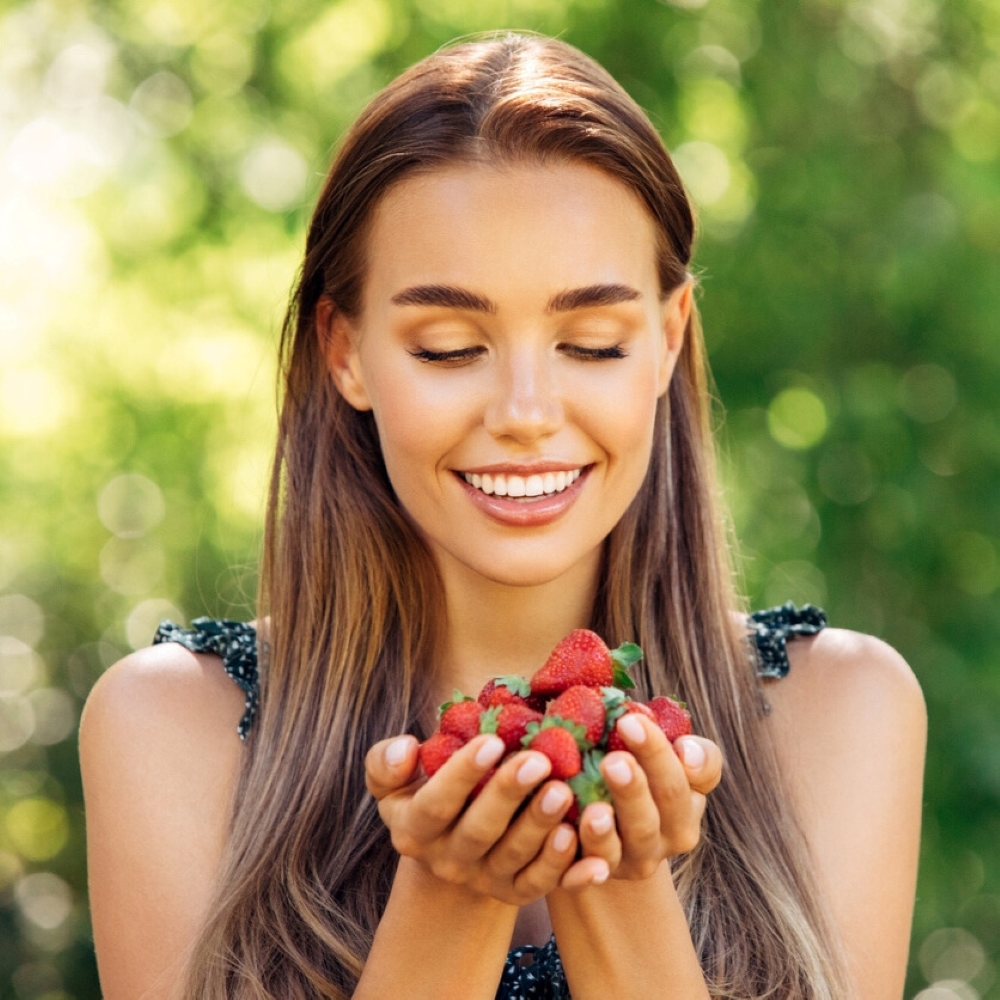service-dietary-advice-oral-health-dentist-wetherill-park Woman smiling while holding fresh strawberries outdoors – promoting healthy diet choices for strong teeth and gums in Wetherill Park.
