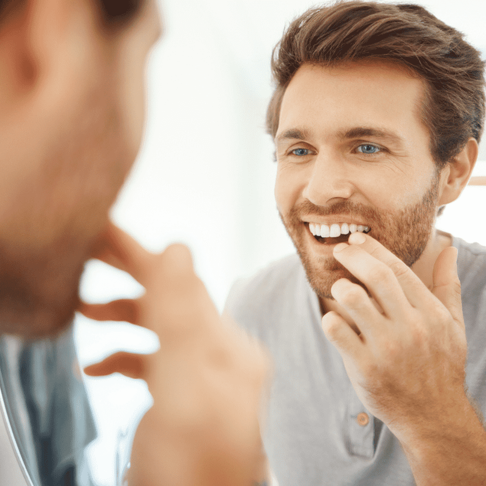 Man checking loose tooth in mirror seeking treatment in Wetherill Park